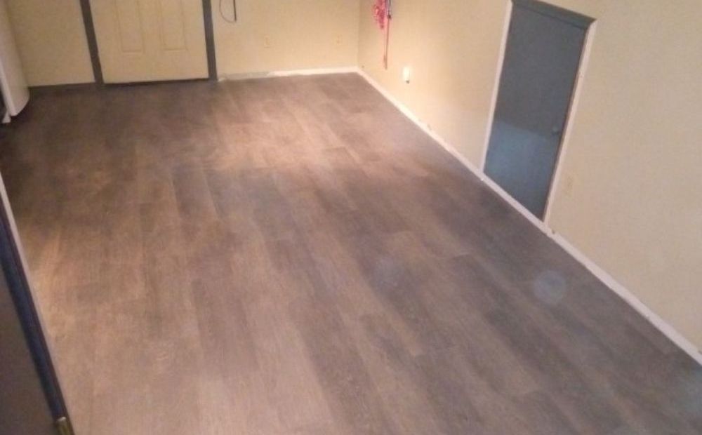 An empty room with newly installed wood-effect plank flooring running to a doorway, with fresh white baseboard.